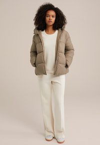 Béžová péřová bunda s kapucňou, obsahujúca prešívané sekcie. Kombinovaná so smotanovými nohavicami a teniskami. Hladká textúra, uvoľnený strih.