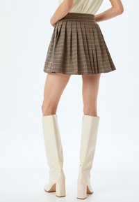 Bruine geruite minirok met plooien, met een hoge taille en een gladde textuur. Gecombineerd met knielange witte blokhakken.