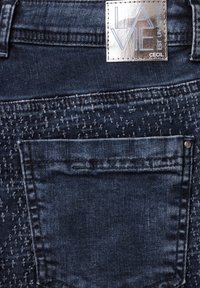 Los jeans de mezclilla azul oscuro presentan un diseño de bolsillo trasero, detalles texturizados y una etiqueta metálica que dice "LA VIE" con "CECIL".