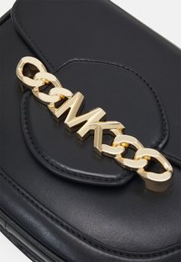 Sac à main en cuir noir avec un design matelassé, une grande chaîne dorée avec les lettres "MK" comme fermoir, et une texture lisse.