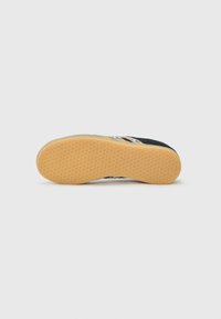 Baskets noires avec une semelle en caoutchouc texturé, arborant un motif en nid d'abeille. Le design comprend un logo blanc sur le côté et un profil bas.