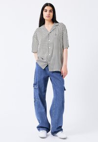 Gestreiftes kurzärmliges Hemd in Schwarz und Weiß, mit Knöpfen, kombiniert mit weit geschnittenen blauen Denim-Cargo-Hosen mit Taschen und einer lockeren Passform.