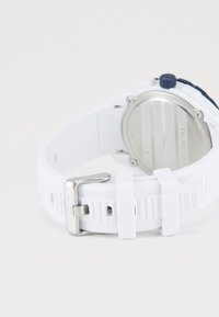 White rubber wristwatch strap with silver buckle and navy blue adjustment knob, showing back metal casing with engraved text.