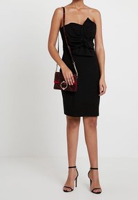 Robe noire sans bretelles avec une silhouette ajustée et des détails froncés. Associée à un sac à main texturé bordeaux et des talons aiguilles noirs.