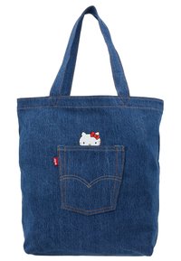 Sac fourre-tout en denim avec deux poignées solides, poche avant ornée d'un personnage de chat blanc avec un nœud rouge, détails de coutures visibles.