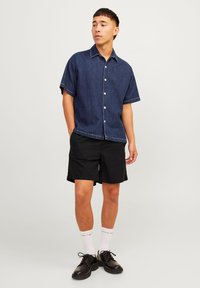 Denim short-sleeve shirt, dark blue, with white buttons and contrasting stitching, paired with black shorts and black shoes.
