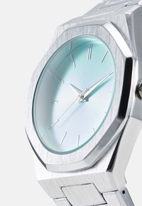 Montre-bracelet octogonale en acier inoxydable argenté avec un cadran dégradé bleu clair, des index horaires argentés minimalistes et une texture brossée sur le boîtier.