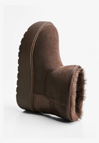 Stivaletto in suede marrone con forma arrotondata, morbido rivestimento in pelliccia e suola in gomma testurizzata con tacco leggero e grip scanalato.