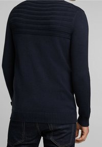 Marineblauwe gebreide trui gezien vanaf de achterkant, met gestructureerde horizontale strepen aan de bovenkant en geribbelde manchetten en zoom.