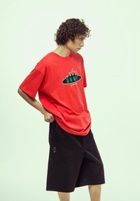 Camiseta de algodón roja con estampado gráfico y llamas, combinada con pantalones cortos negros. El conjunto presenta un corte relajado y un detalle mínimo.