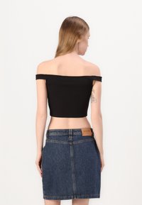 Top corto nero scollato sulle spalle abbinato a una gonna di denim, con un'etichetta in vita e un design aderente.