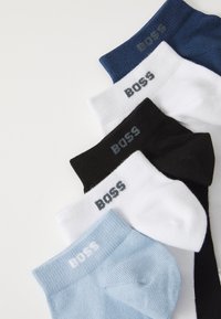 Cinq paires de chaussettes à chevilles en marine, blanc, noir et bleu clair. Toutes présentent une texture côtelée et le logo 'BOSS' dans des couleurs contrastantes sur les poignets.