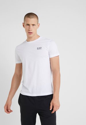 T-shirt in cotone bianco con maniche corte, scollo rotondo, caratterizzato da un piccolo logo EA7 nero sul lato sinistro del petto. Texture liscia, vestibilità regolare.