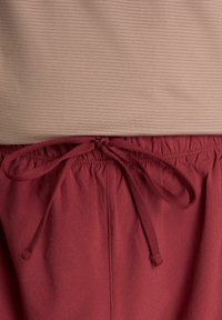 Top marrone chiaro a coste sopra pantaloncini con fascia elastica color marrone scuro e coulisse. I pantaloncini presentano piccoli fori uniformemente distanziati per la texture.