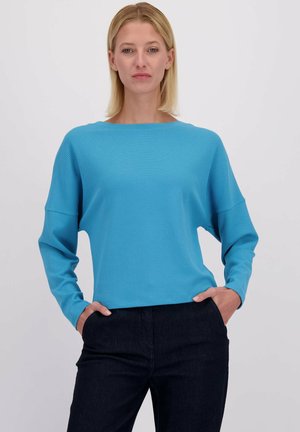 Blauwe geribbelde lange mouwen top met een brede halslijn, losse pasvorm en verlaagde schouders, gecombineerd met donkere broeken. Glad textuur en casual ontwerp.