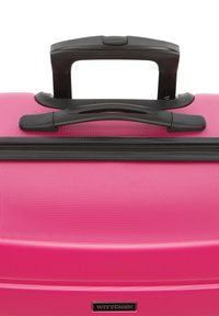 Valigia rigida di un vivace colore rosa, con superficie testurizzata, manico nero retrattile e chiusura a zip. Presenta una placca con il logo.
