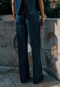 Tamsiai mėlynos plačios kojelės džinsai su taškeliais. Audinys turi tekstūrinį paviršių, matomi galiniai kišeniai.