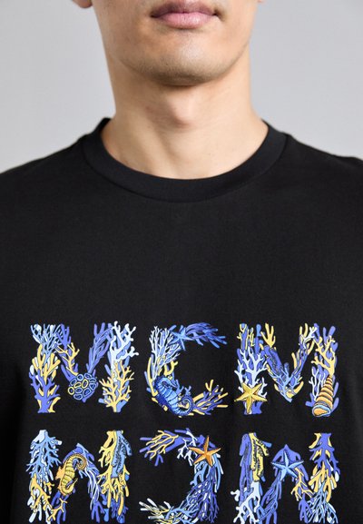 T-shirt en coton noir avec des graphiques colorés de corail et de vie marine en bleu, jaune et orange disposés autour du texte "MCM."
