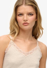 Camisola color crema con bordo in pizzo sullo scollo e spalline regolabili, realizzata in morbido tessuto a coste.