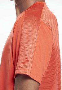 Camiseta deportiva naranja con textura de malla en las mangas, escote redondo y cuerpo fabricado con material ligero y transpirable.