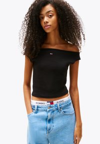 Fekete, vállt szabadon hagyó cropped top rövid ujjakkal, amelyet magas derekú világoskék farmernadrággal párosítottak, márkás derékkal.
