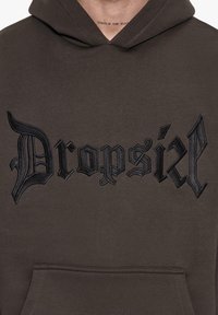 Barna kapucnis pulóver, fekete hímzett "Dropsial" felirattal, elülső zsebbel és a pamutszövethez hasonló textúrával.