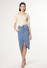 Top in maglia a coste beige con maniche corte abbinato a una gonna di jeans a vita alta, dotata di uno spacco frontale e chiusura a 5 bottoni.