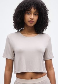T-shirt court beige avec une texture côtelée, manches courtes et col rond. Porté avec un bas beige assorti, présentant une coupe décontractée.