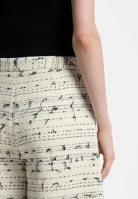 Shorts en crêpe tissée crème avec motifs abstraits noirs, dotés d'une finition texturée et d'une coupe large. Haut côtelé noir partiellement visible.