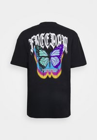 Svart bomullströja med en stor, färgglad fjärilsdesign i blått och lila, med texten "FREEDOM" ovanför och "TRANSFERENCE" nedanför.