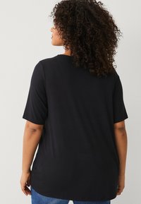T-shirt nera a maniche corte in una vestibilità rilassata, con una texture liscia e un colletto rotondo, con cuciture visibili e un design semplice.