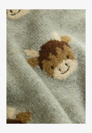 La tela verde presenta un tejido texturizado con un patrón esponjoso de cabezas de vaca marrones sonriendo, acentuado por orejas y detalles de color crema.