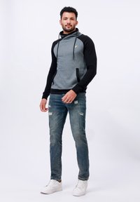Szary i czarny hoodie z kapturem, wyposażony w przednie kieszenie i sznurki do regulacji. Noszony z przetartymi niebieskimi dżinsami i białymi sneakersami.