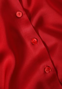 Red satin shirt with a smooth texture, featuring four matching round buttons along the front. Close-up view highlighting fabric sheen.