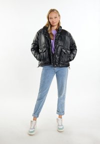 Jachetă puffer neagră cu un finisaj lucios, două buzunare frontale, un guler înalt și tiv ajustabil. Asortată cu blugi de culoare albastră deschisă și adidași multicolori.
