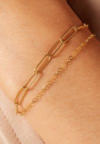 Juego de pulseras de oro que incluye una cadena de eslabones alargados y una cadena de eslabones ovalados delicados, ambas con un acabado pulido, descansando sobre una superficie de piel.