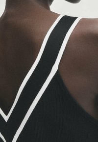 Canotta nera con spalline bianche a contrasto, un motivo a maglia texture e un design a schiena a V che mette in risalto l'area delle spalle.