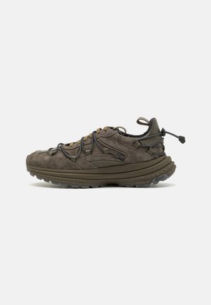 Adidași din suede, de culoare maronie închisă, cu o finisare texturată, având șireturi elastice, tab de prindere și talpă Vibram pentru o tracțiune îmbunătățită.