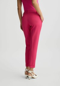 Fukszia színű, slim fit szabású nadrág, cuffos szegéllyel és hátsó zsebekkel. Anyaga simának tűnik, a strukturált dizájn hangsúlyozza a karcsú sziluettet.