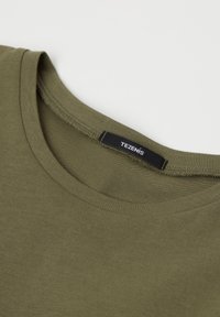 Olivově zelené bavlněné tričko s kulatým výstřihem a plochým švem. Černá etiketa s nápisem "TEZENIS" je viditelná blízko výstřihu.