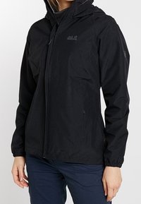 Svart vattentät jacka med huva, med en framzipper och elastiska manschetter. Designen inkluderar en logotyp på bröstet och sidofickor.