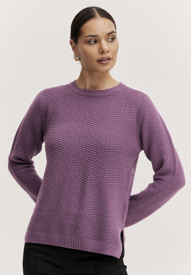 Lila, strukturierter Strickpullover mit rundem Halsausschnitt, langen Ärmeln und seitlichen Schlitzen. Aus einem leichten, atmungsaktiven Material.