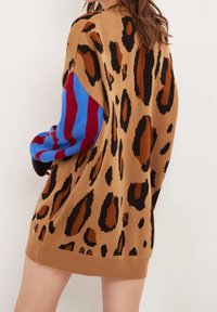 Stickad klänning med en brun bas och svarta och bruna leopardfläckar, röda och blå randiga ärmar samt ribbade muddar.