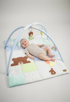 Bébé allongé sur un tapis d’éveil aux couleurs pastel avec des motifs d’ours et de ballon, sous un arceau bleu avec des peluches suspendues dont un ours.