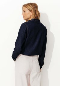 Chemise en denim foncé avec un col volanté, présentant des manches longues et des poignets boutonnés, associée à un pantalon en velours côtelé rose clair.