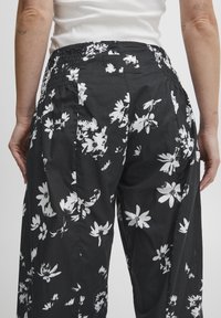 Svarta byxor i lätt tyg med blommigt vitt mönster, elastisk midja och avslappnad passform.