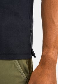 Navyblaues, strukturiertes Kurzarmshirt mit seitlichen Belüftungsöffnungen und Markenetikett, kombiniert mit olivgrünen Shorts. Verfügt über ein geripptes Design und einen lässigen Schnitt.