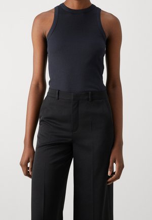 Femme portant un débardeur moulant sans manches en côte bleu marine foncé, rentré dans un pantalon noir tailleur taille haute.