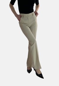 Beige flared broek met een hoge taille, een gladde textuur en zijzakken, gecombineerd met zwarte lakleren hoge hakken.