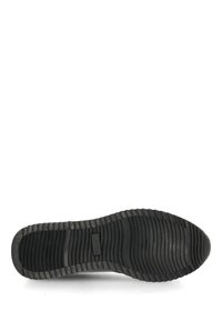 Svart gummisul med ett strukturerat, ribbat mönster. Har en liten logotypetikett och en slät kant längs kanterna.